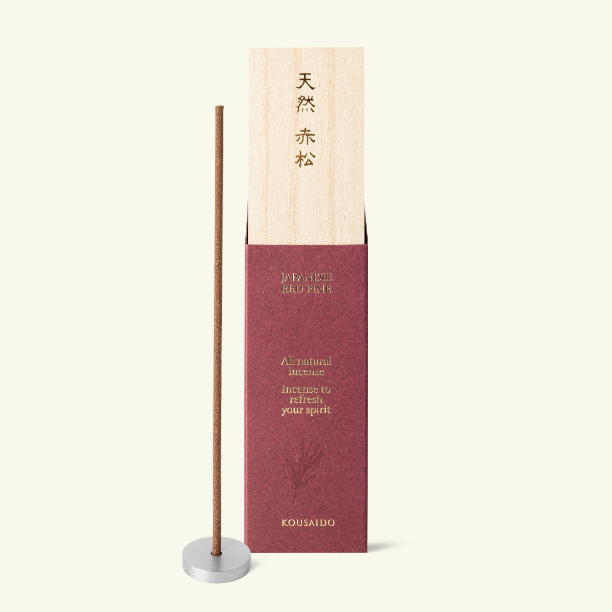 Kousaido Japanese Red Pine incense in a burgundy box beside a single incense stick standing in a round metal holder.